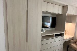 Clóset multifuncional de pared beige con cajones y puertas, espacio para televisión y accesorios diseñado por California Closets